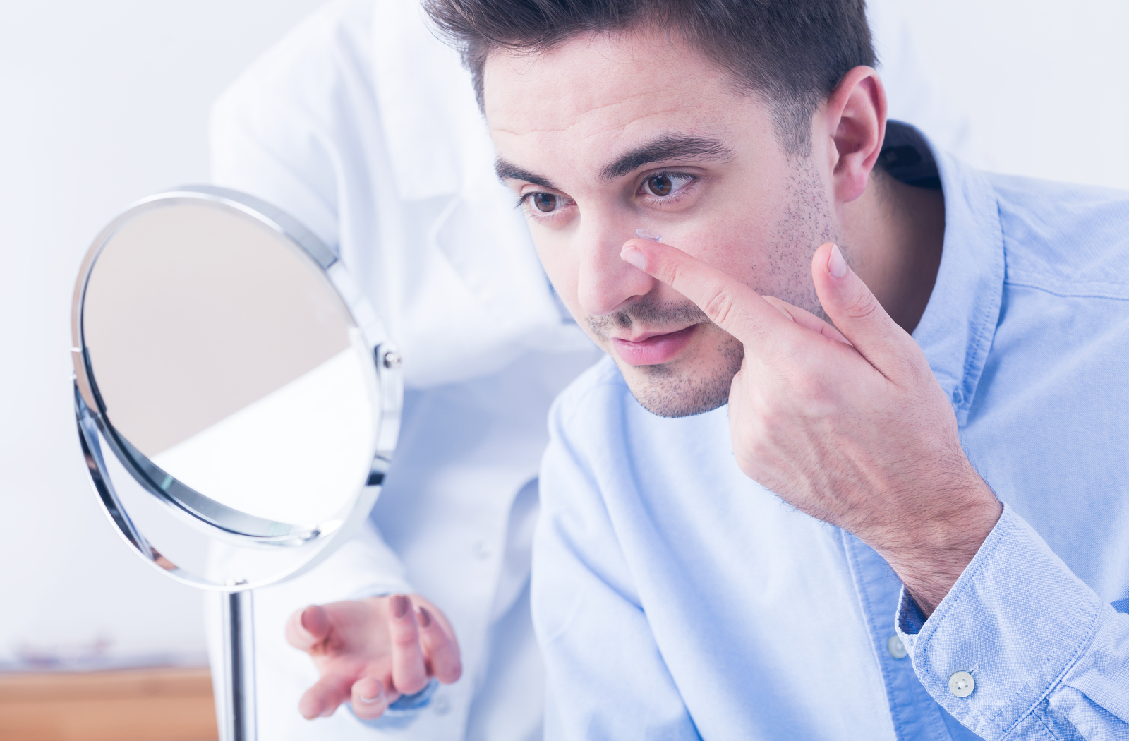 Young man at optometrist office putting in contact lens during fitting