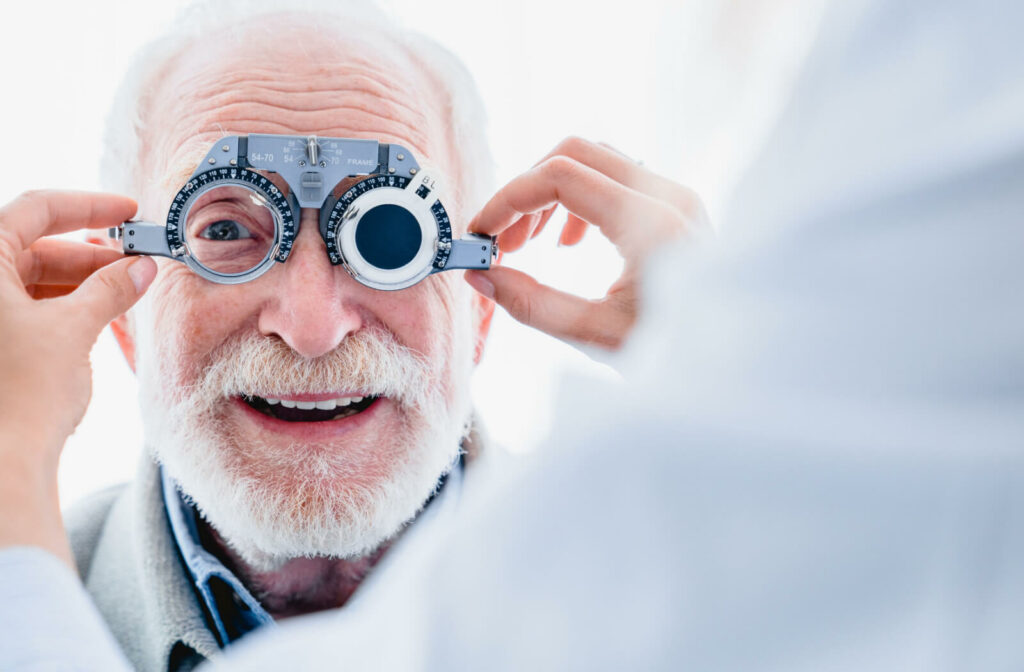 An old man wearing a phoropter held by the hands of a female optometrist measuring the patient's vision