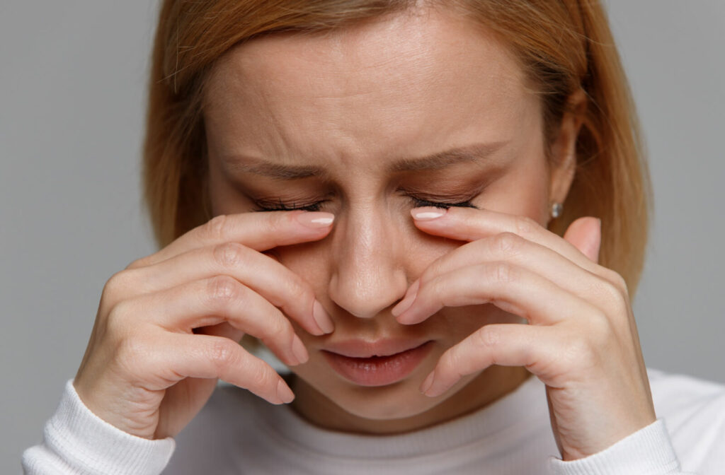 A woman rubbing her itchy dry eyes with contact lenses on .