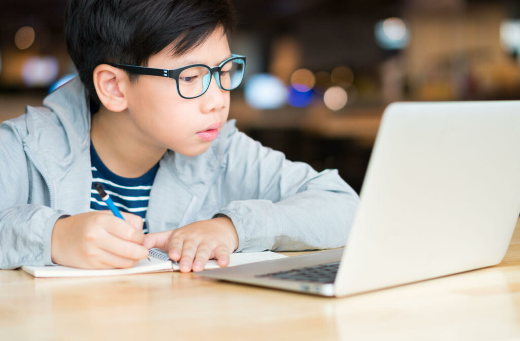 A boy is wearing blue light-blocking glasses while using a computer laptop during his online class.