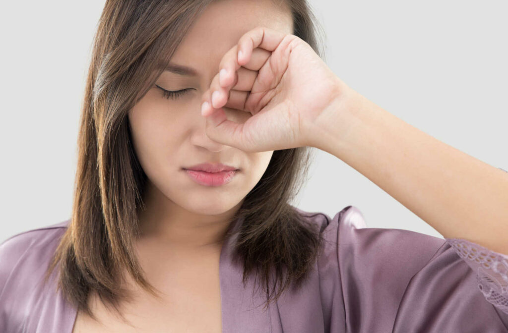 A close-up of a woman in a nightdress rubbing her eye with the back of her hand.