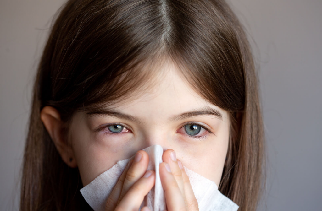 A young girl is blowing her nose in a napkin, with red eyes due to allergies