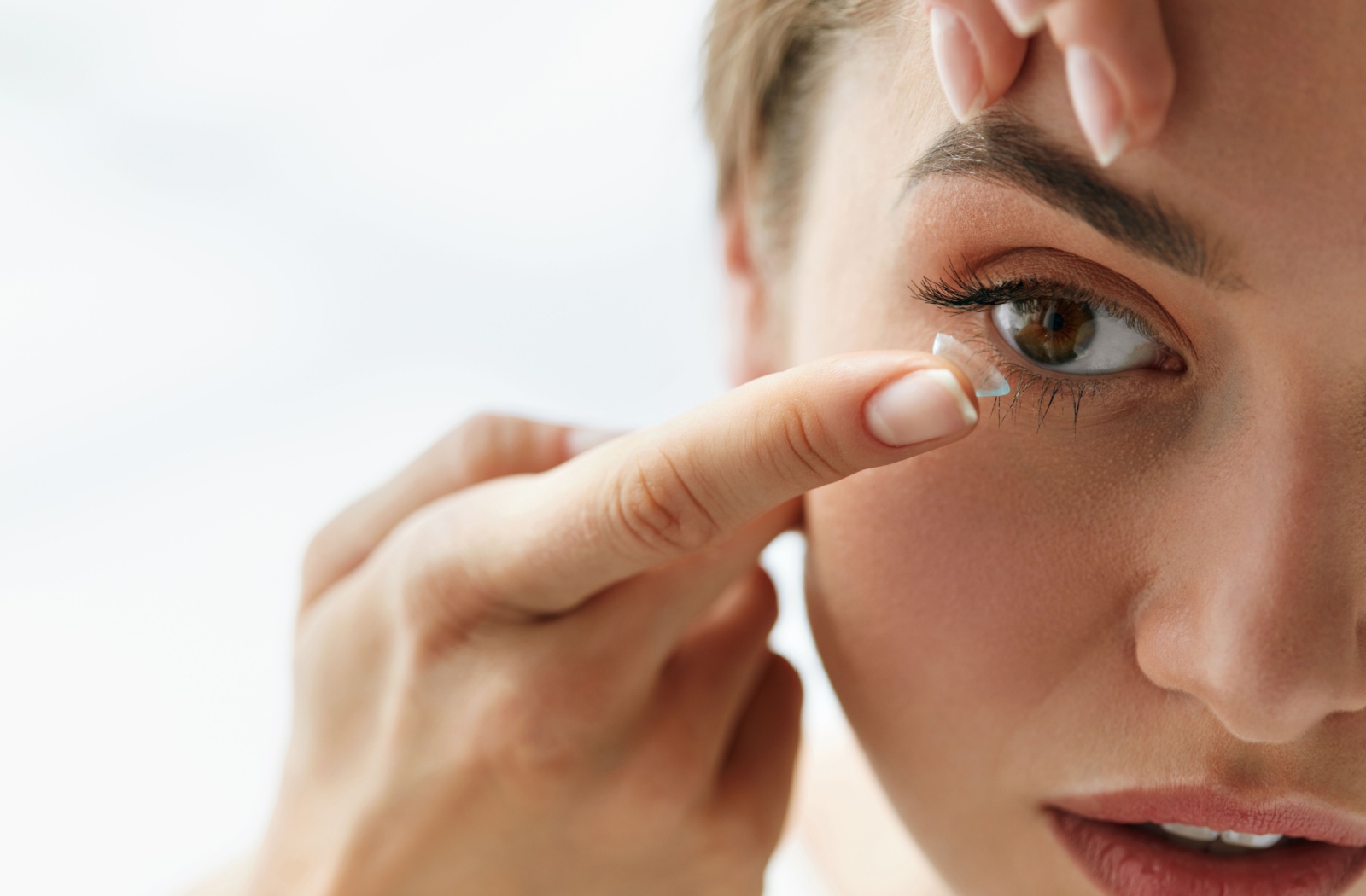 A woman using her left index finger to pull her eyelid up while she puts a contact lens on her right eye with her right hand