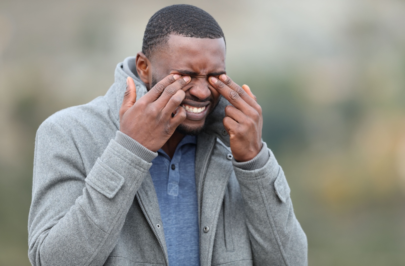 Young man with a stressed expression pressing at his closed eyes with both hands.