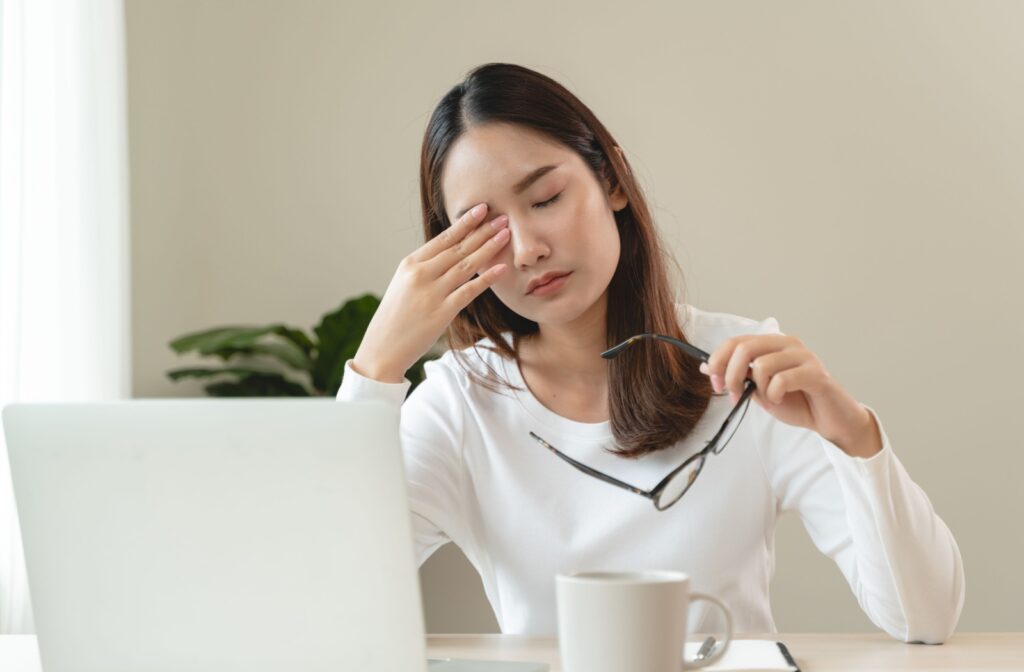 A person in front of their computer rubbing their eyes due to dry eye symptoms.