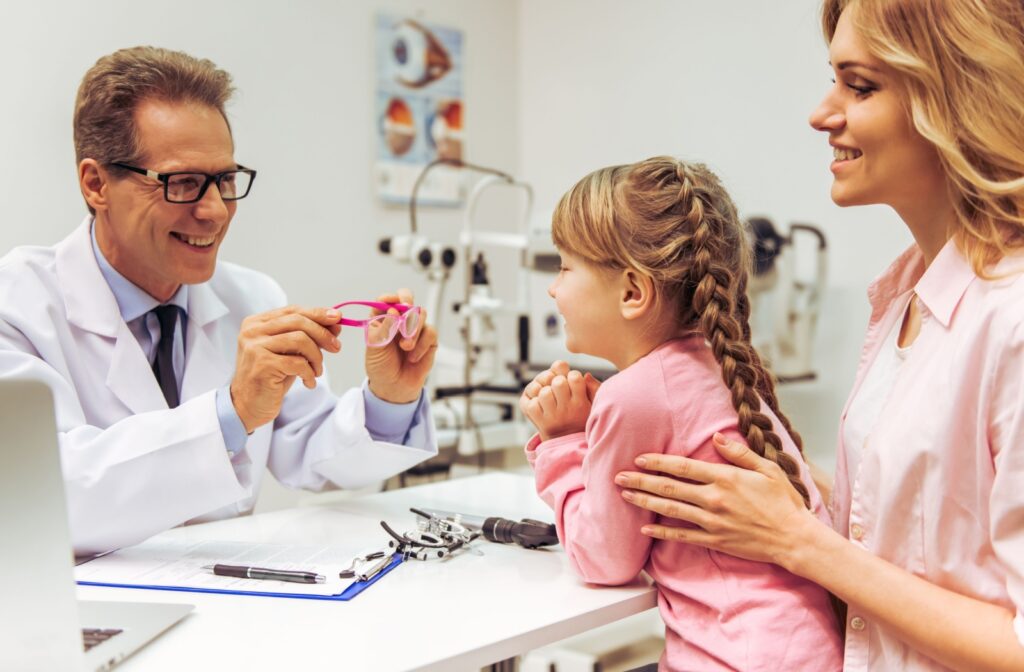 An optometrist talks to their young patient and parent about myopia control treatments while holding a pair of myopia glasses.