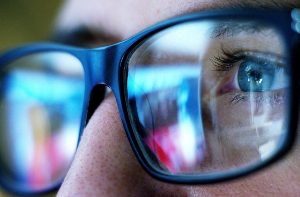 A close up of someone wearing glasses and their computer screen is reflected in the lens